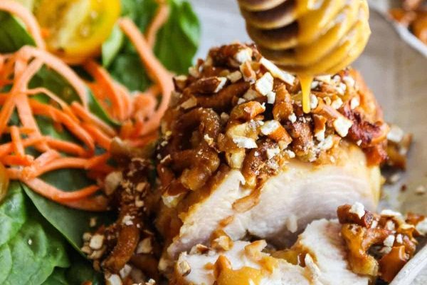 A piece of chicken with honey and nuts on a plate.