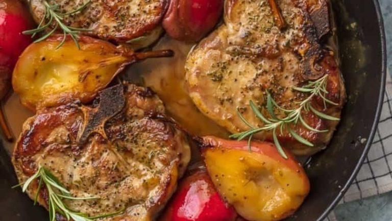 Pork chops in a skillet with apples and sprigs of rosemary.
