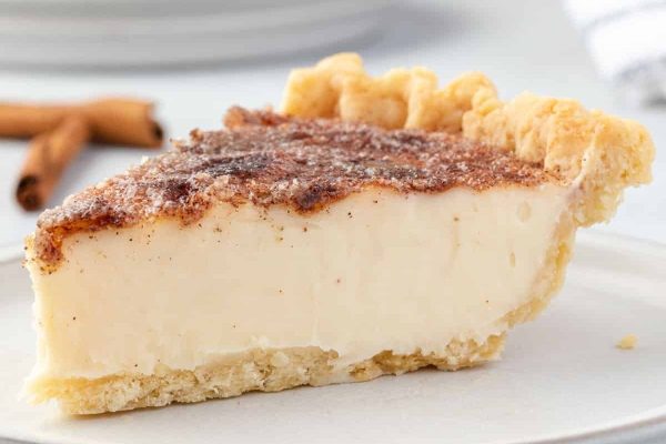 A slice of pie on a plate with cinnamon sticks.