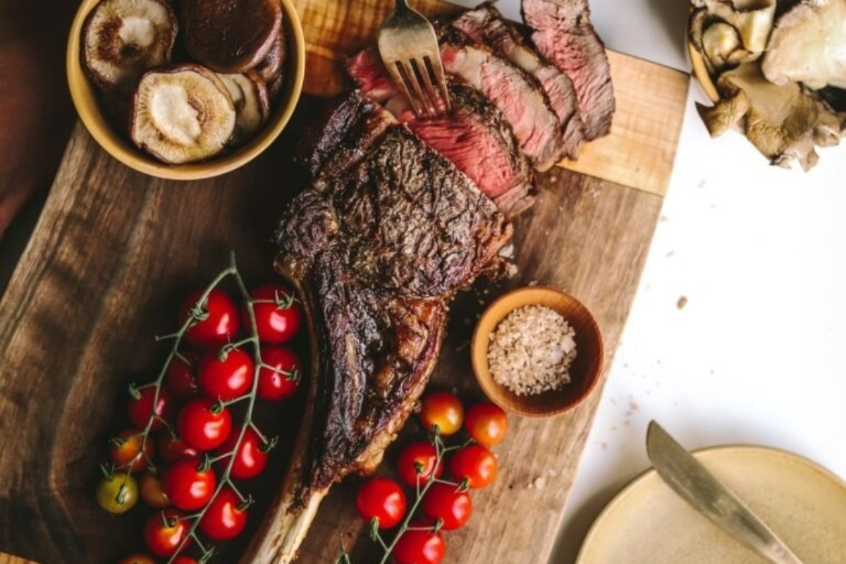 A mouthwatering dinner party main featuring a succulent steak served on a cutting board alongside fresh tomatoes and mushrooms.