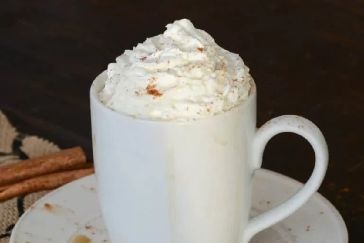 A white mug of hot cocoa with whipped cream and cinnamon sticks.