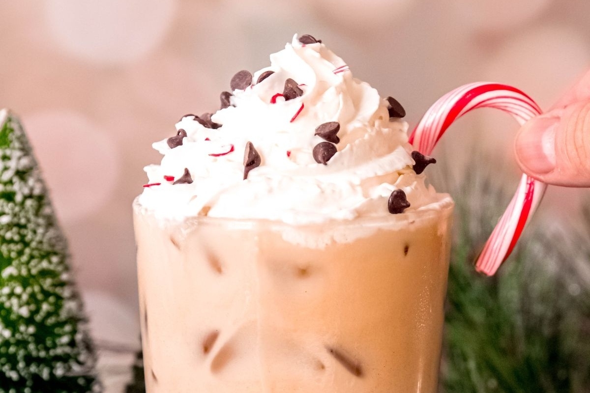 A Starbucks-inspired holiday recipe featuring a person holding a candy cane iced coffee topped with whipped cream and a candy cane.
