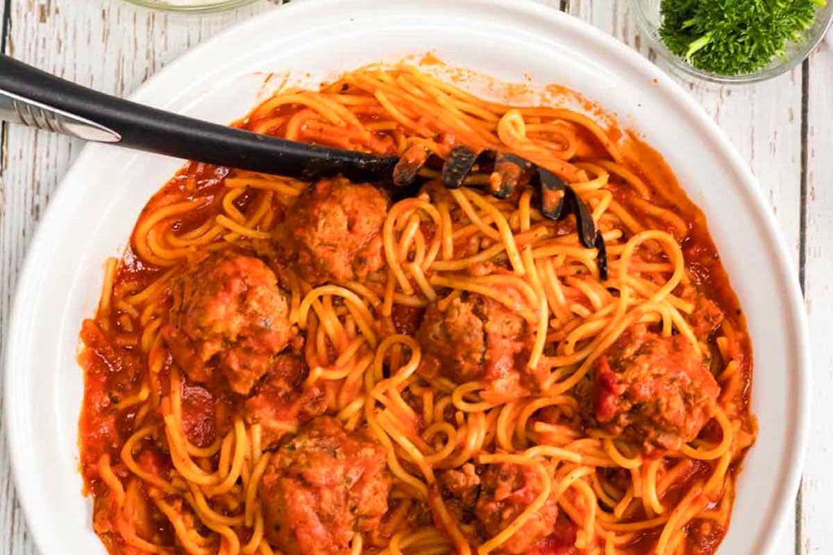 Spaghetti and meatballs in a white dish with a fork.