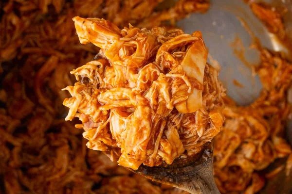 A spoonful of shredded chicken in a pan.