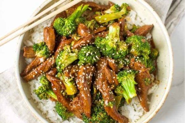 A bowl of beef and broccoli stir fry with chopsticks.