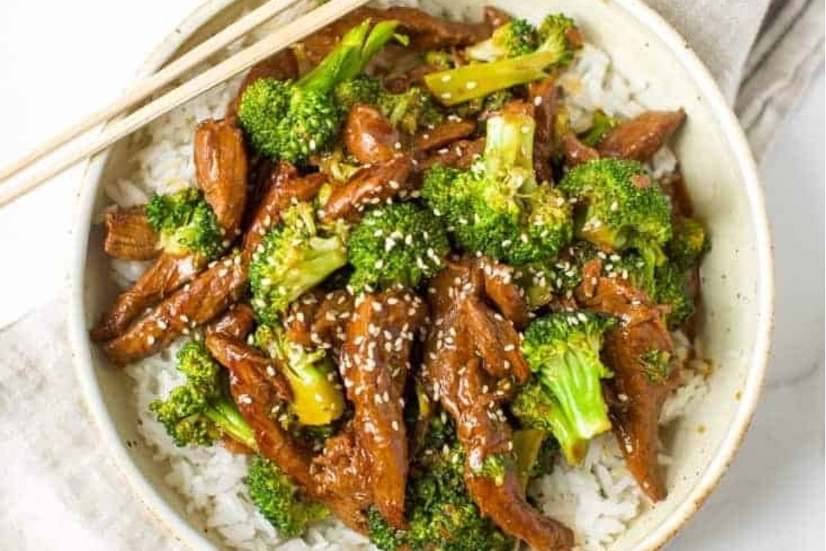 A bowl of beef and broccoli stir fry with chopsticks.