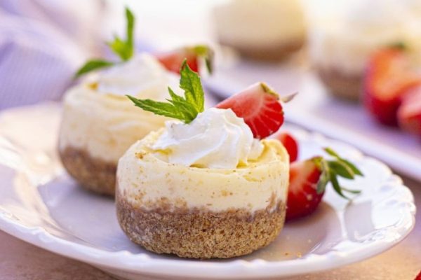 A plate of mini cheesecakes topped with strawberries and whipped cream.