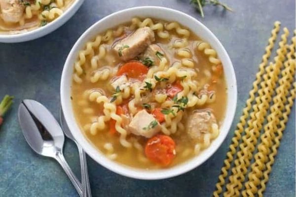 A bowl of chicken noodle soup with noodles and carrots.