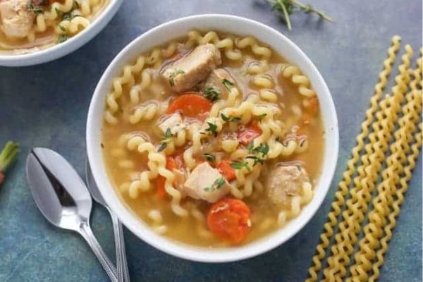 A bowl of chicken noodle soup with noodles and carrots.