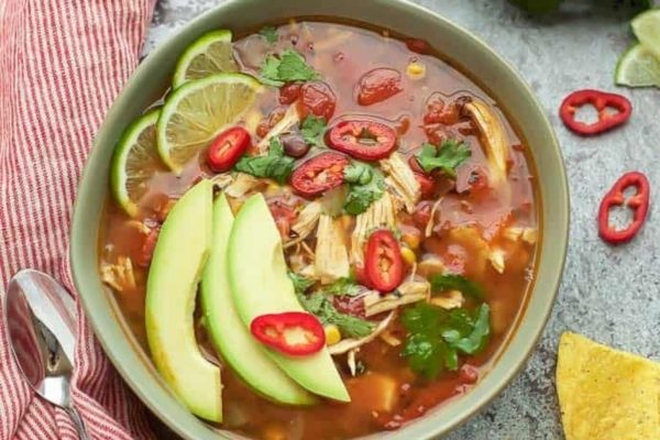 A bowl of mexican chicken soup with avocado, lime and tortillas.