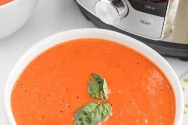 A bowl of tomato soup in front of an instant pot.