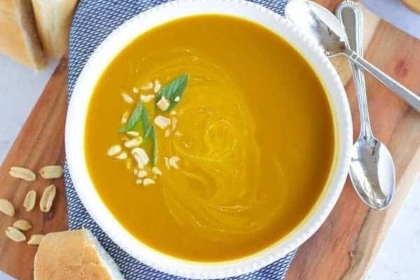 A satisfying bowl of pumpkin soup - a soup made with few ingredients - served alongside freshly baked bread on a rustic cutting board.