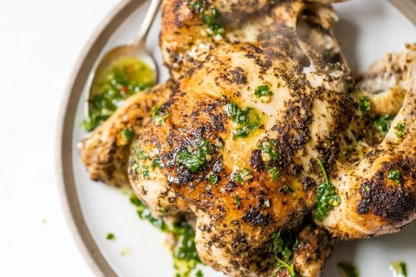Roasted chicken with herbs on a white plate.