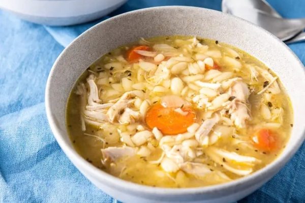 Chicken noodle soup in a bowl on a blue tablecloth.