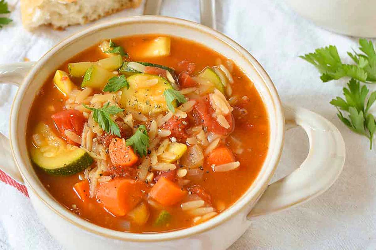 A bowl of soup with vegetables and bread.
