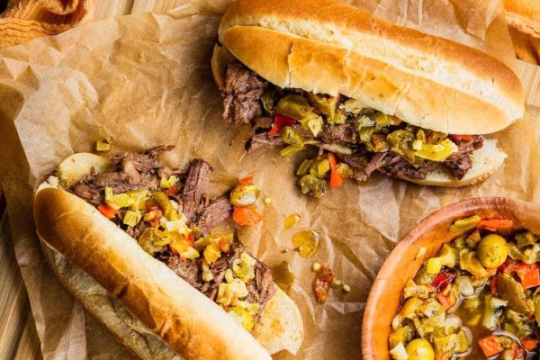 Two sandwiches with meat and vegetables on top of a piece of paper.