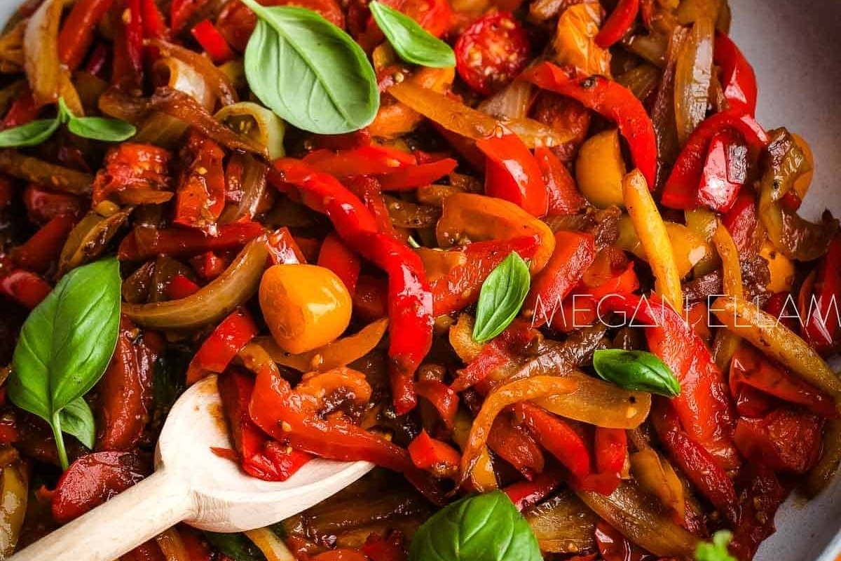 Italian roasted red peppers in a skillet with basil leaves.