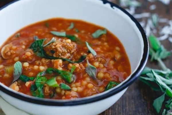 A bowl of soup with meat and sprigs of sage.