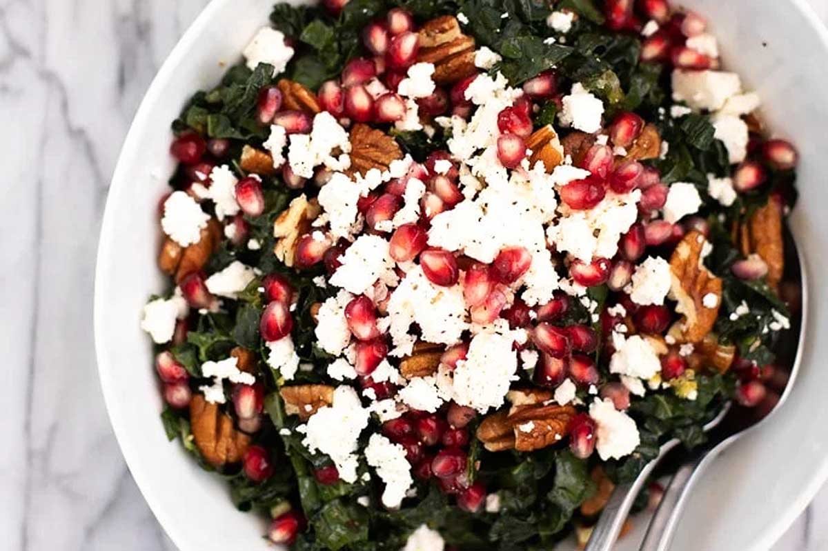 A bowl of kale and pomegranate salad with feta and pecans.