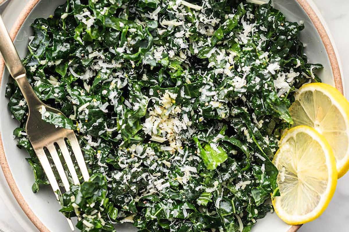 A bowl of kale salad with lemon wedges and parmesan cheese.