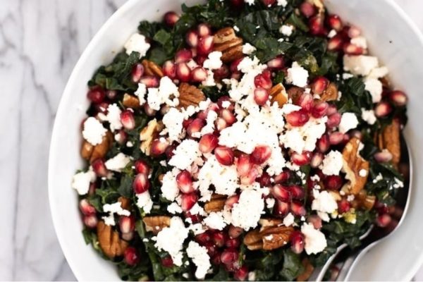 A colorful Christmas salad featuring kale and pomegranate, topped with feta and pecans.