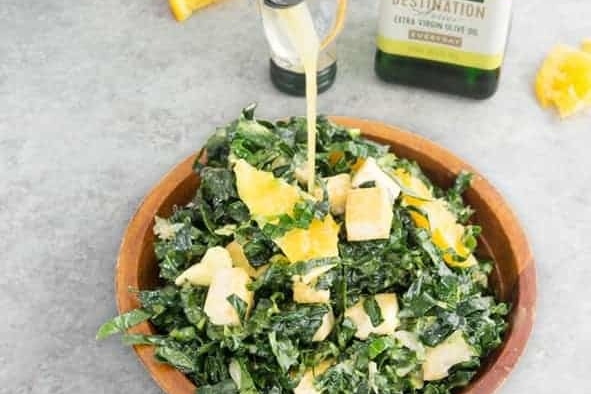 A bowl of kale salad with orange juice being poured over it.