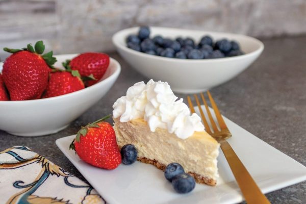 A slice of cheesecake with whipped cream and berries on a plate.