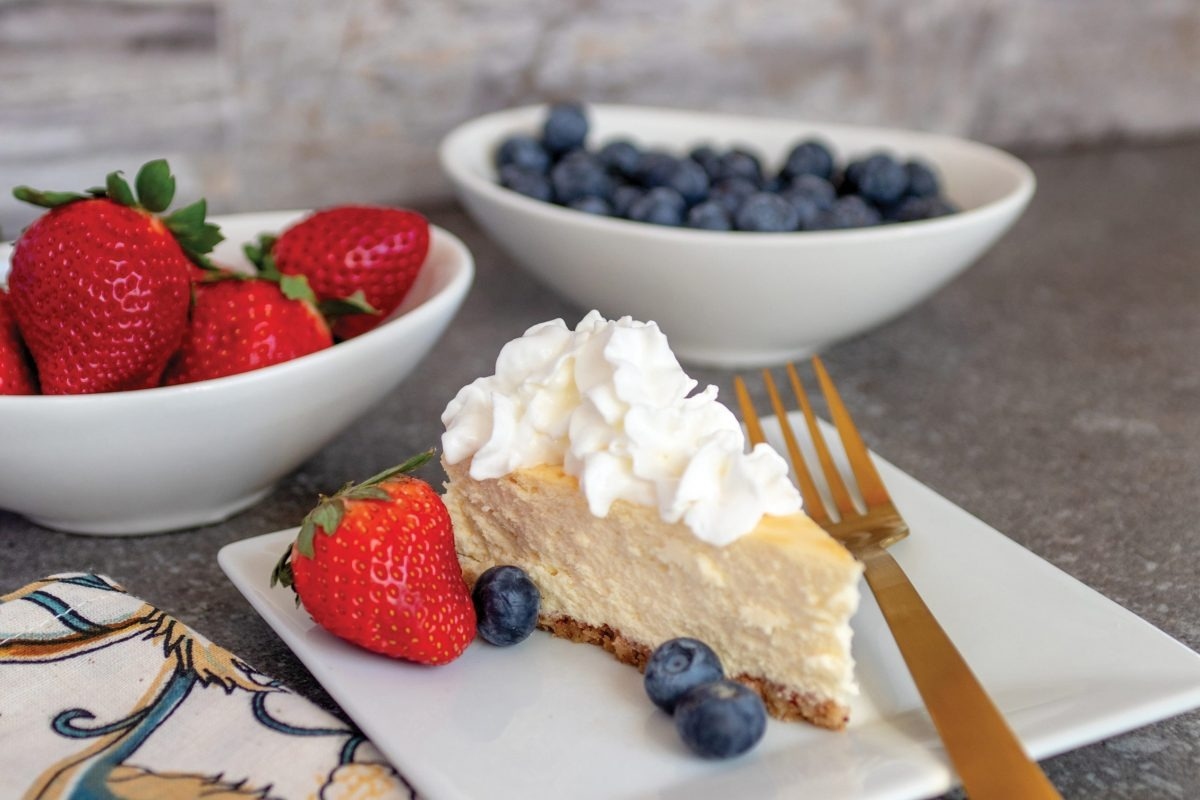 A slice of cheesecake with whipped cream and berries on a plate.