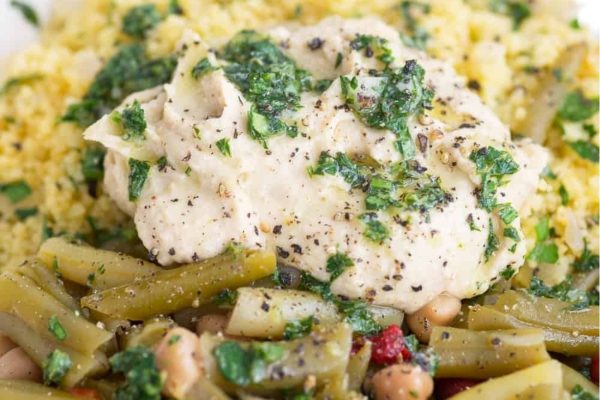 Colorful couscous and green beans with tender chicken on a plate.