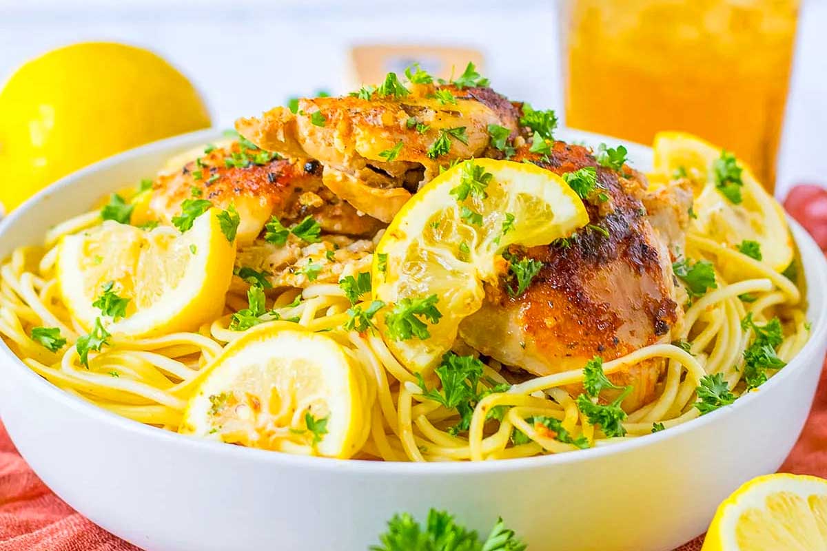 A bowl of pasta with chicken and lemons.