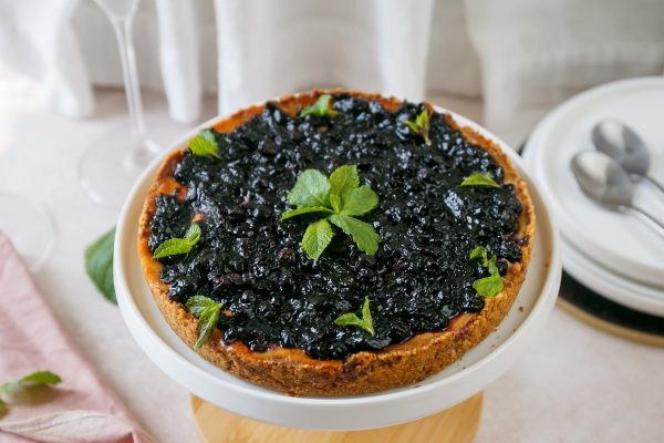 A blueberry cheesecake on a white plate with a glass of wine.