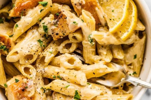A kid-friendly chicken parmesan pasta, garnished with lemon wedges, served in a white bowl.