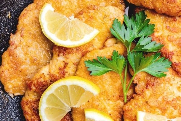 Fried chicken with lemon slices and parsley in a skillet.