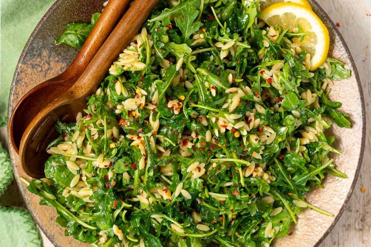 An Italian arugula salad recipe served with lemon wedges and wooden spoons.