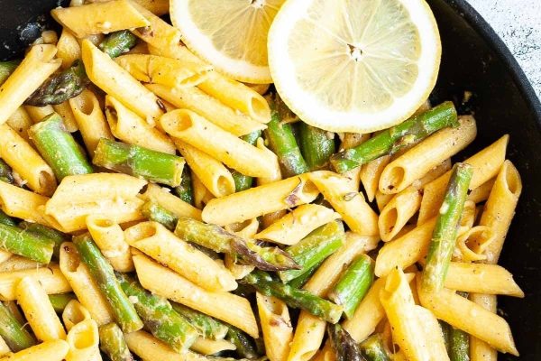 Penne pasta with asparagus and lemon wedges in a skillet. This recipe combines the deliciousness of pasta, specifically penne, with the freshness of asparagus and a hint of tang