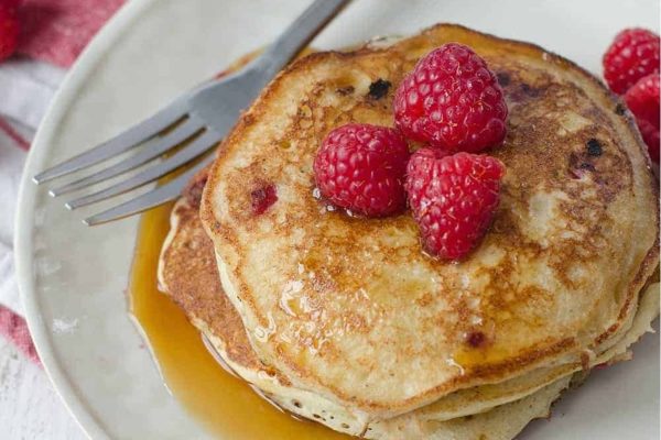A stack of pancakes with raspberries and syrup on a plate.