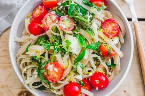 A bowl of pasta with tomatoes, spinach and feta cheese.