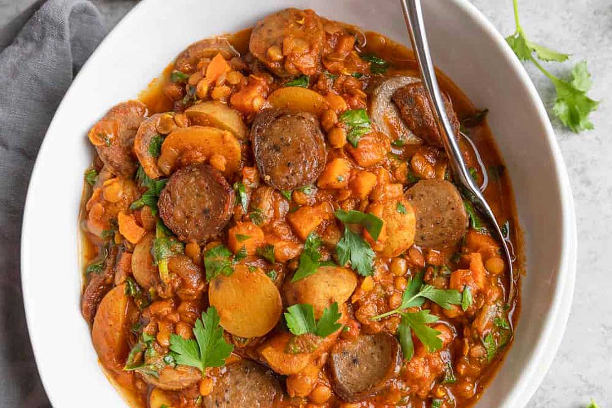 Sausage and potato stew in a white bowl with a spoon.