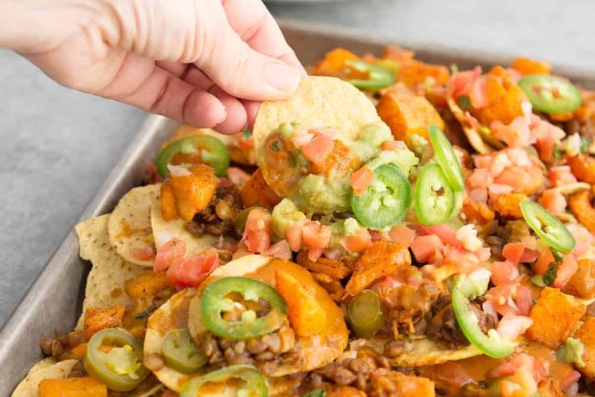 A hand grabbing nachos from a baking sheet.