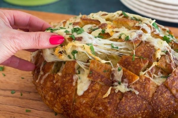 A person is dipping a hand into a cheesy bread.