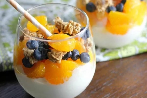 A glass of yogurt with oranges, blueberries and granola.