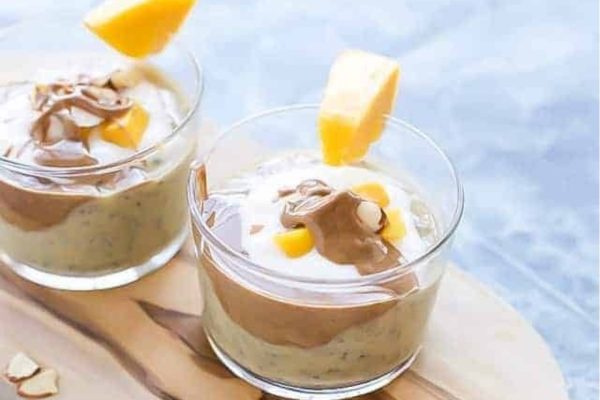 Two glasses of mango pudding topped with whipped cream, perfect for breakfast or meal prep.