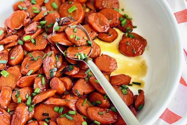 Roasted carrots in a white bowl with a spoon, perfect for your Thanksgiving feast or potluck gathering. Plus, this cheap and delicious side dish is sure to please everyone!