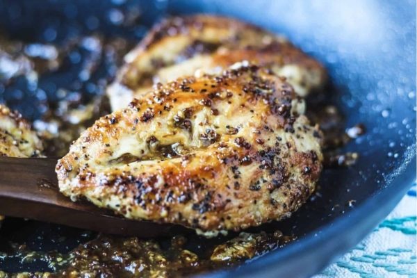 Chicken breasts in a frying pan with a wooden spoon.