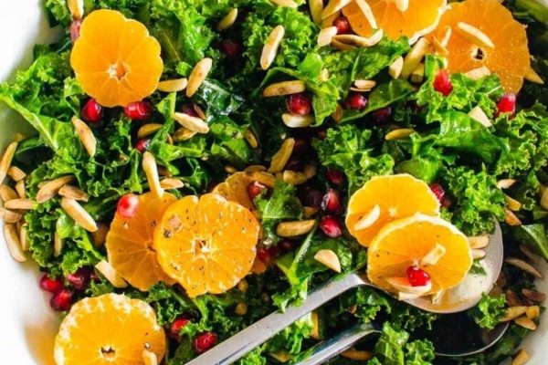 A bowl of kale salad with oranges and pomegranate.