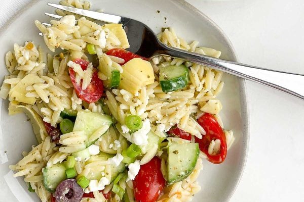 A plate of pasta salad with tomatoes, cucumbers and olives.
