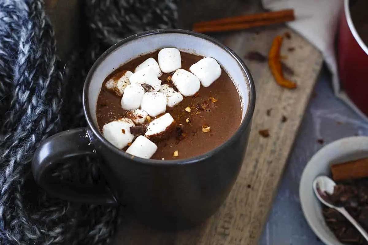 A mug of hot chocolate with marshmallows and cinnamon sticks.