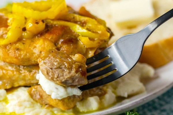 A fork is holding a plate of meat and mashed potatoes.