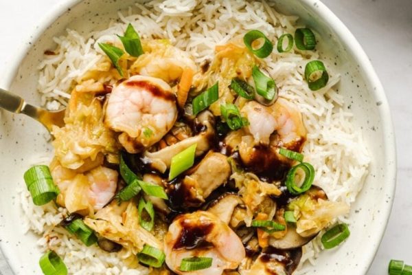 A bowl of rice with shrimp and green onions.