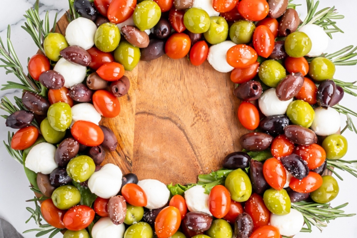 A wreath of olives and tomatoes on a wooden cutting board, perfect for a charcuterie spread.